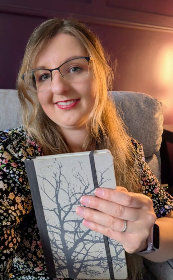 A selfie of the author smiling and holding up a closed notebook, celebrating a writing milestone.