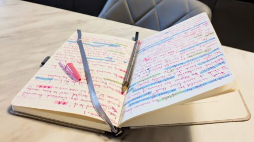 An open notebook filled with pages of handwritten notes in red ink, heavily marked with various shades of blue and green highlighter.