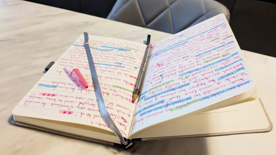 An open notebook filled with pages of handwritten notes in red ink, heavily marked with various shades of blue and green highlighter.