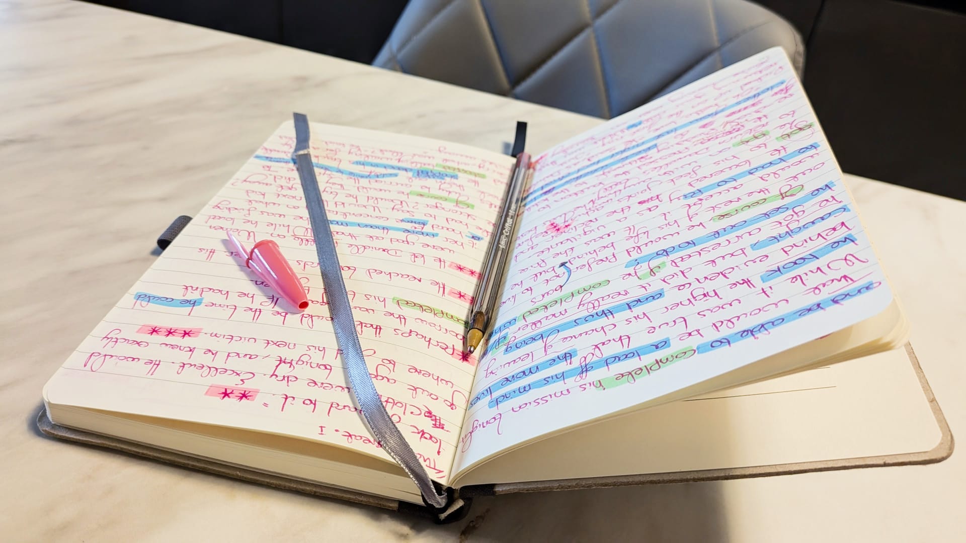 An open notebook filled with pages of handwritten notes in red ink, heavily marked with various shades of blue and green highlighter.
