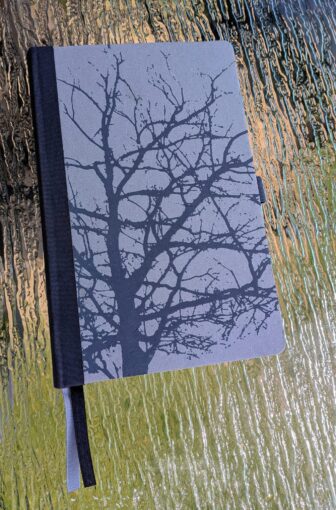 A closed, dark-colored notebook featuring a subtle silhouette of a tree on its cover, hinting at mystery.