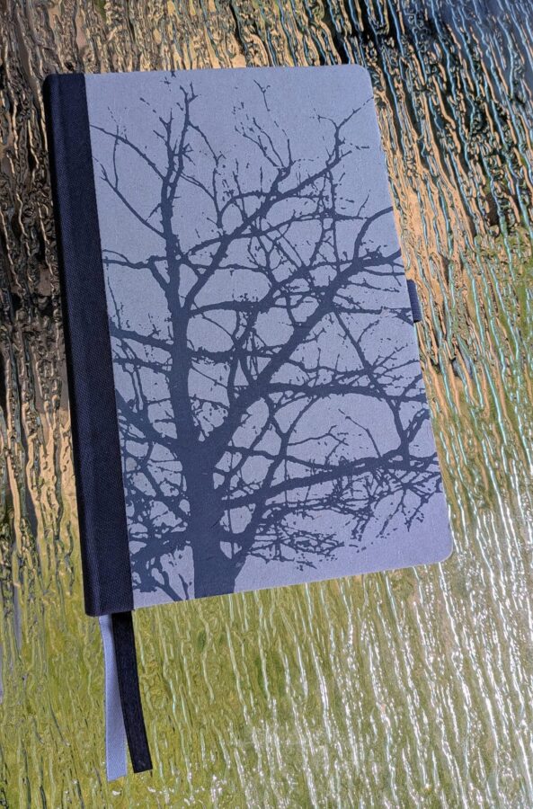 A closed, dark-colored notebook featuring a subtle silhouette of a tree on its cover, hinting at mystery.