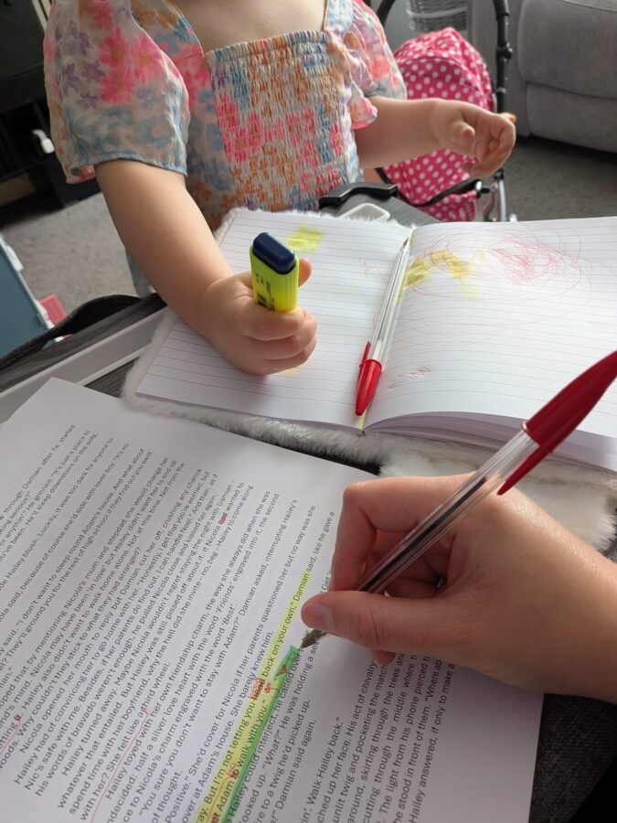 A candid shot of an author focused on editing an A4 sheet of paper, while their three-year-old daughter happily "edits" her own drawing with a bright highlighter beside them.