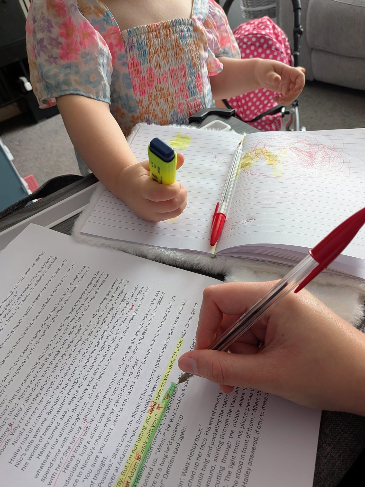 A candid shot of an author focused on editing an A4 sheet of paper, while their three-year-old daughter happily "edits" her own drawing with a bright highlighter beside them.